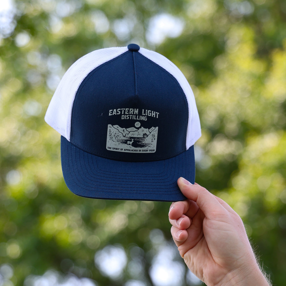 Navy Blue and White Trucker Hat with Eastern Light Distilling Branding on Outdoor Background