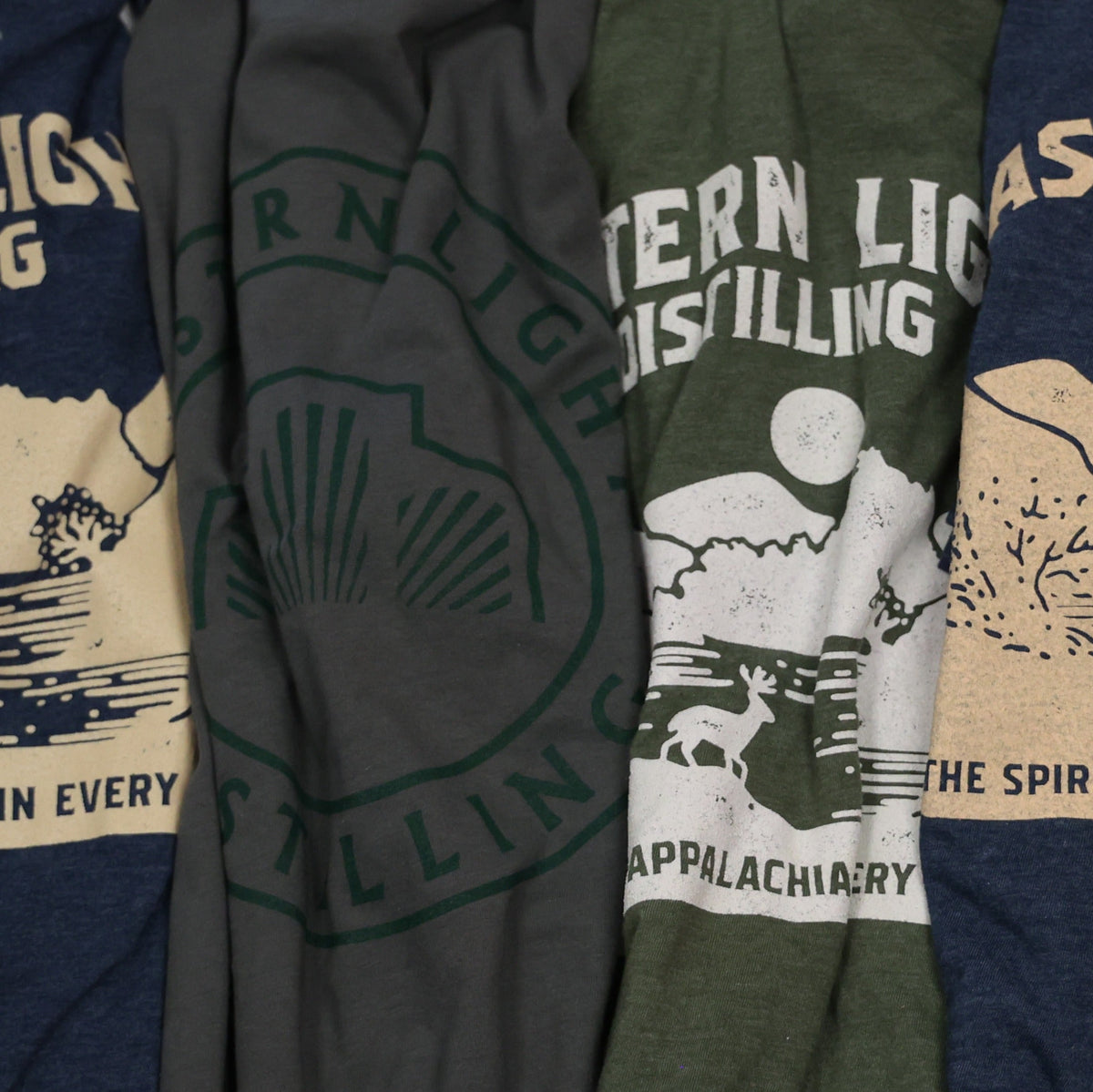 Four Eastern Light Distilling T-shirts Side by Side, in Navy, Gray, and Green, Eastern Light Distilling Merchandise Lifestyle Products