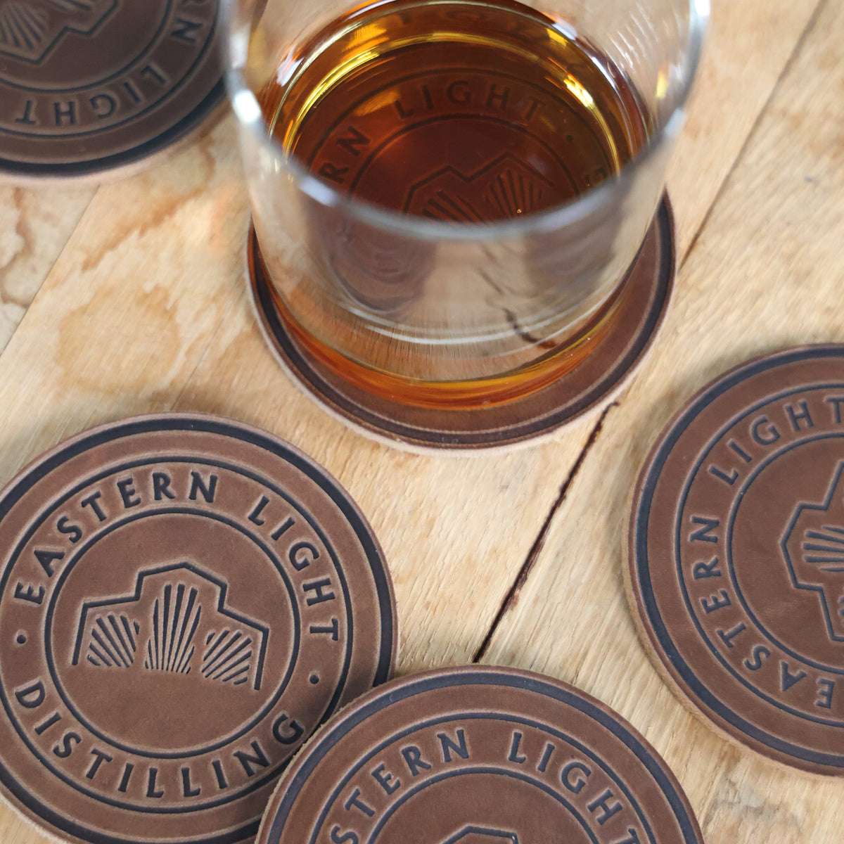 Bourbon Glass on Leather Eastern Light Distilling Coaster and Bourbon Barrel Background with More Leather Coasters Surrounding